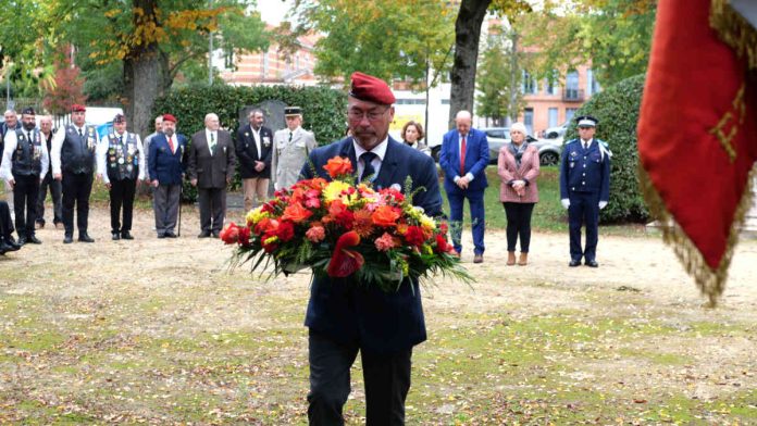 Éric Guichard portant une gerbe de fleurs lors de la cérémonie des 20 ans de l'ADACME
